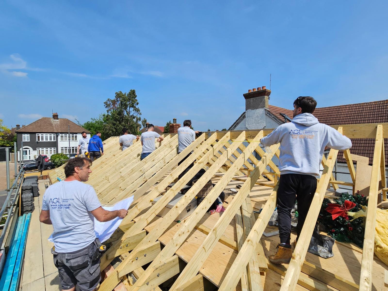 AGL team working across the new timber rafters of a replacement roof, one holding drawings.