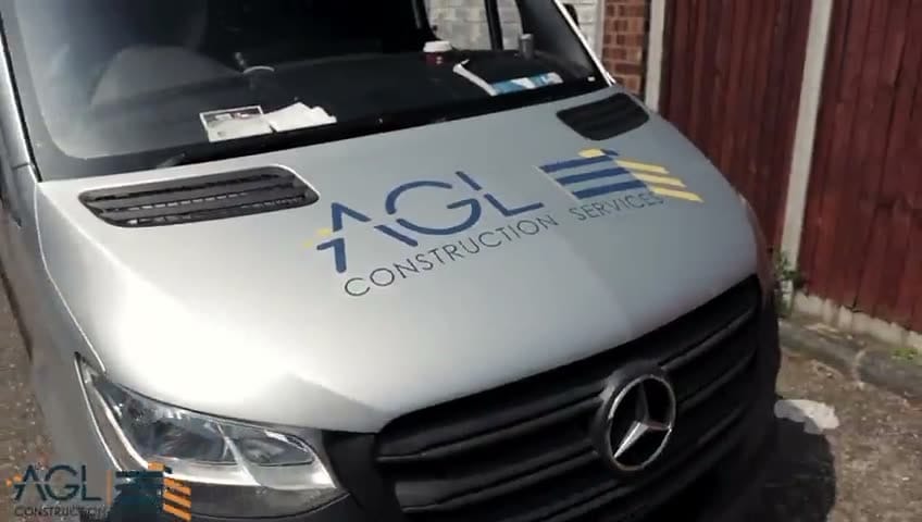 AGL Construction Services logo on the bonnet of a silver work van parked beside a fence.