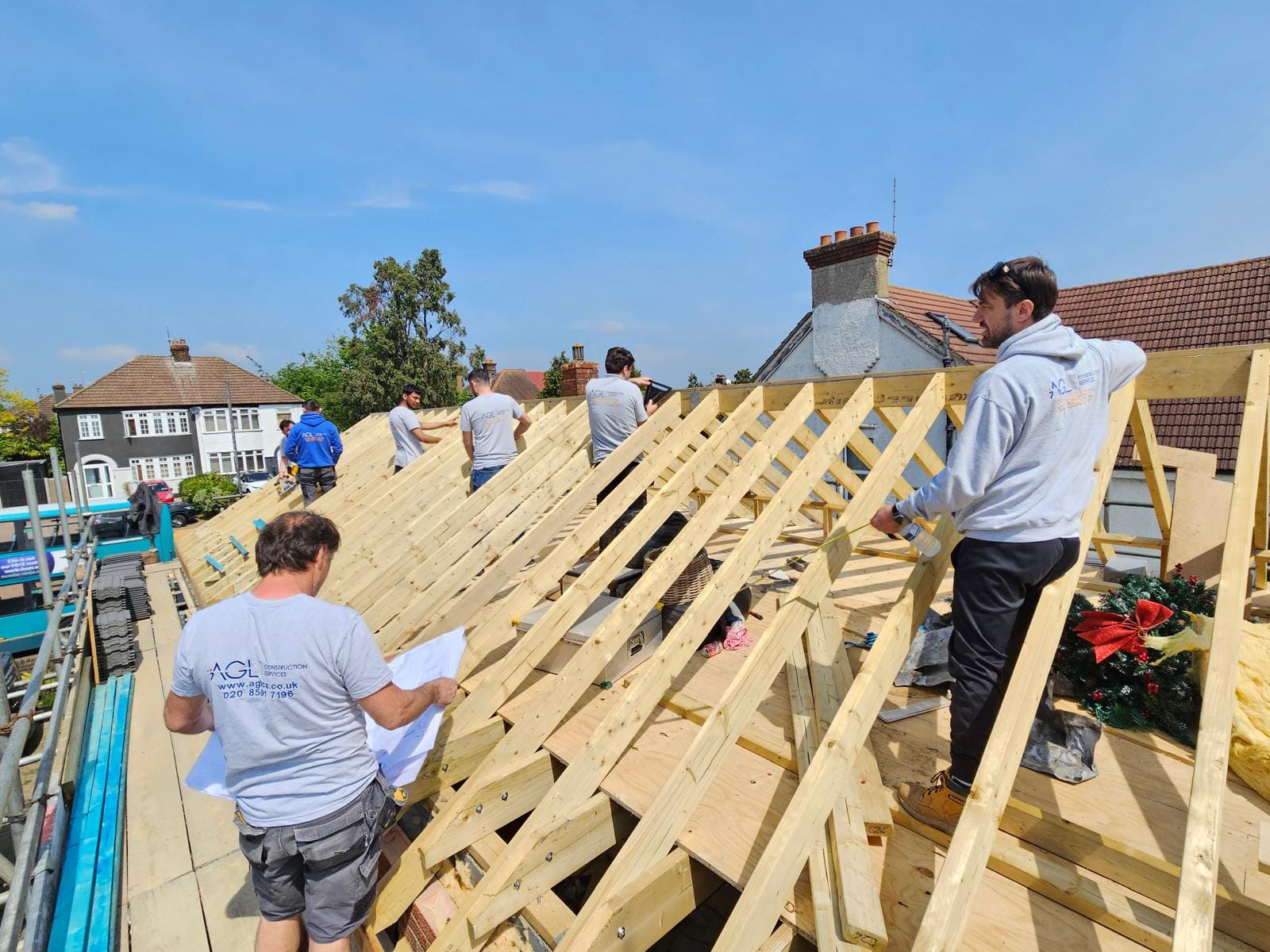 AGL team working on the new timber rafters of a replacement roof against a clear blue sky.