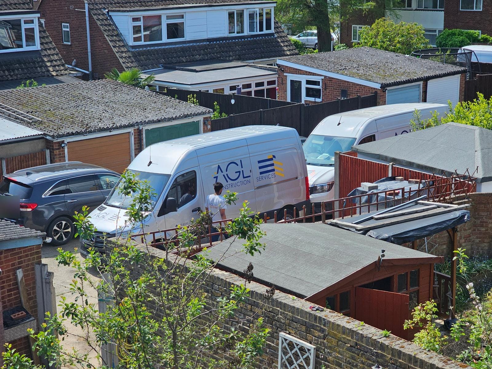 AGL vans parked on a rear service road beside garages and back gardens, seen from above.