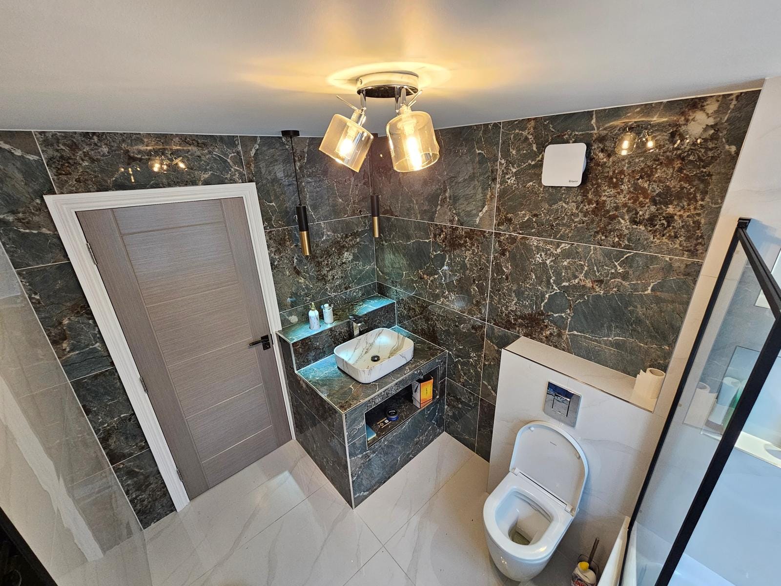 Bathroom with dark-green marble-effect wall tiles, a vessel basin on a tiled plinth and a wall-hung WC.