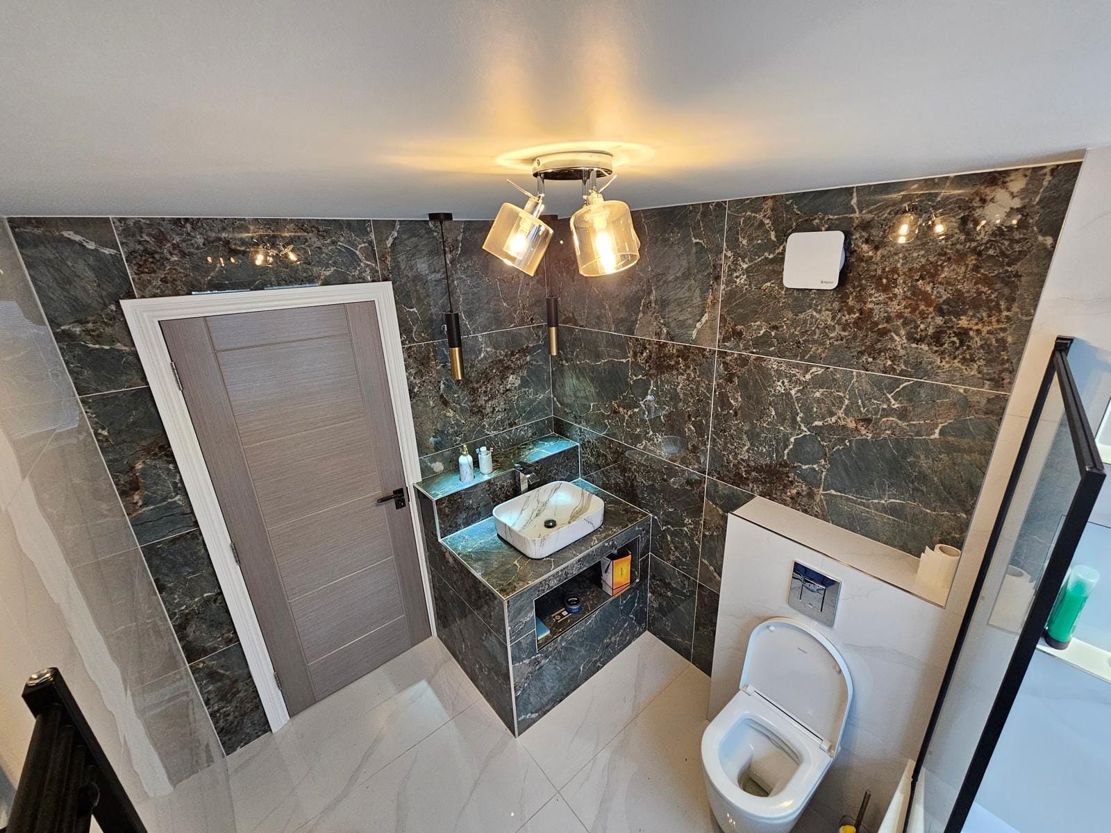 Bathroom from the doorway with dark-green marble-effect walls, a vessel basin on a plinth and a wall-hung WC.