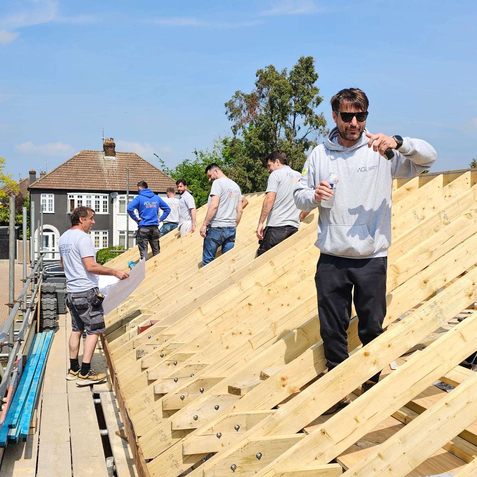 Carpenter in an AGL hoodie standing on the new rafters with a water bottle, as the team works along the roof.