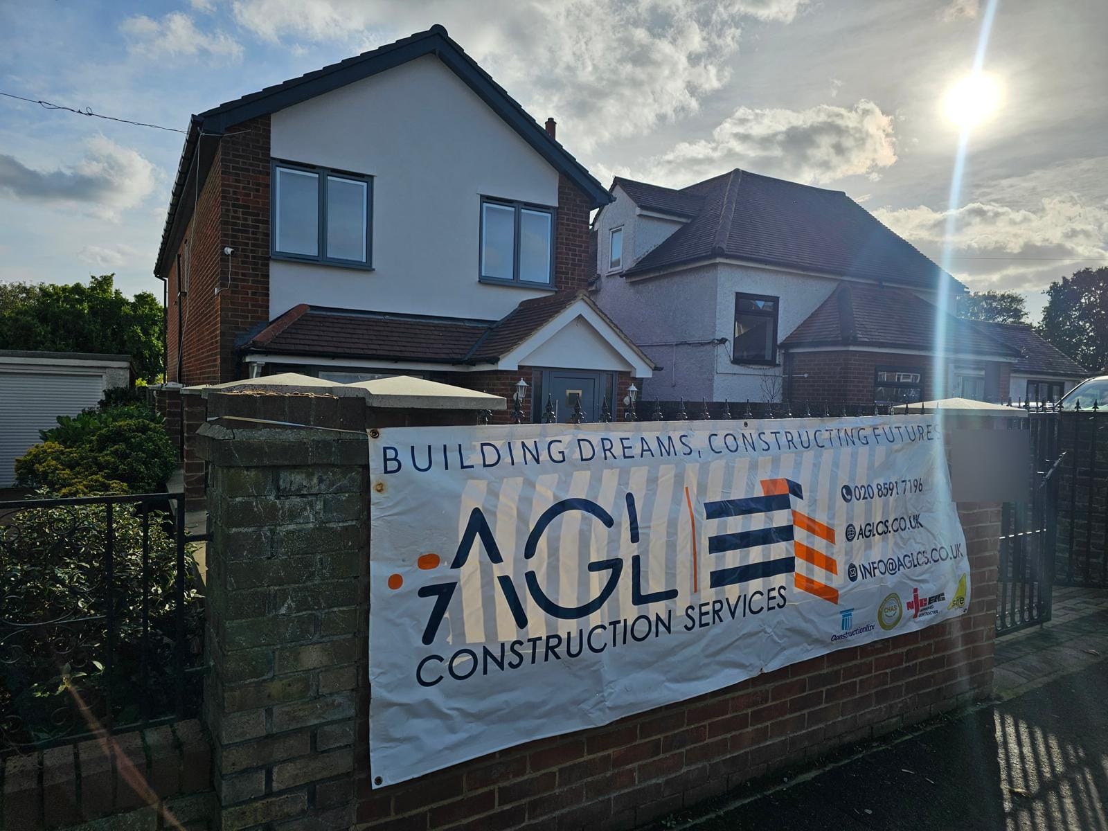 Completed house behind a brick front wall and railings, with an AGL Construction Services banner on the wall.