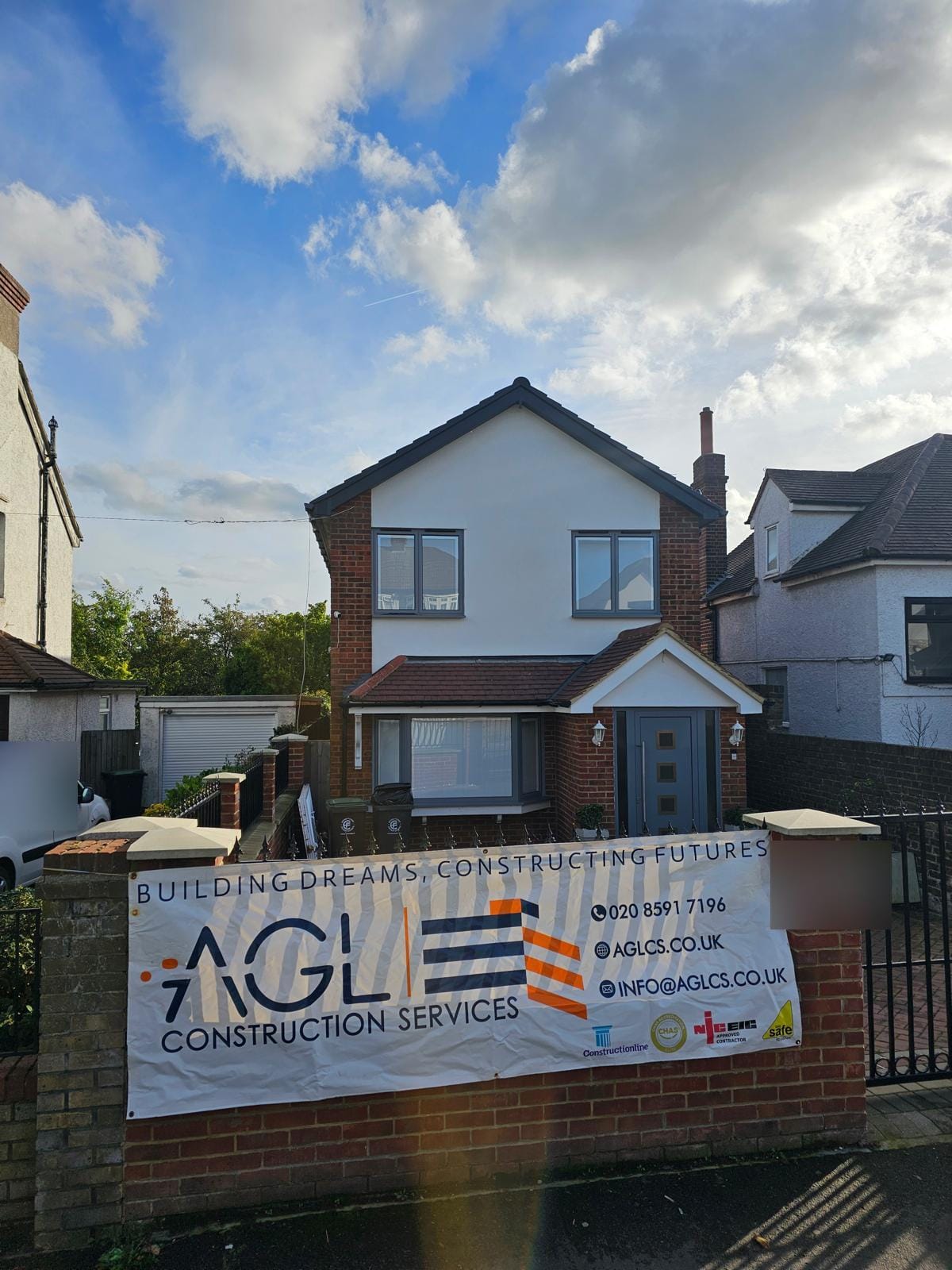 Completed two-storey house with a white-rendered first floor and grey windows, and an AGL banner on the front wall.