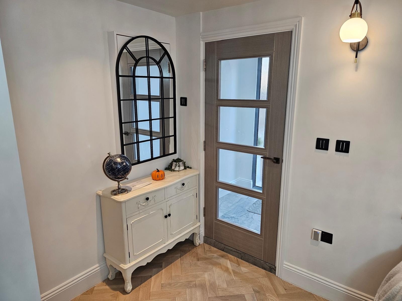 Hallway with a four-panel glazed internal door, a white console table, an arched mirror and herringbone flooring.