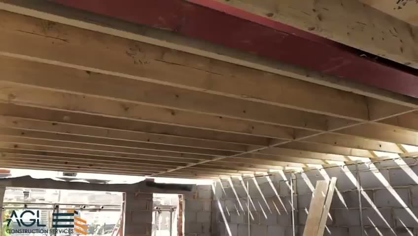 New timber joists and a red steel beam above blockwork walls, seen from below during building works.
