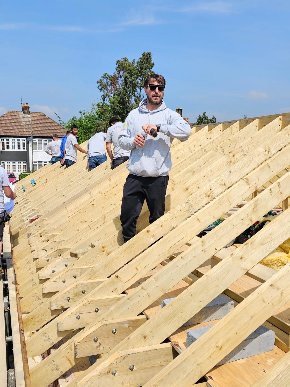Operative in sunglasses and an AGL hoodie standing on the new rafters, with the team at work behind.
