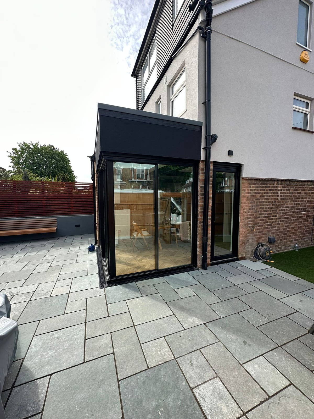 Single-storey rear extension with black-framed corner glazing and sliding doors opening onto a grey sandstone patio.