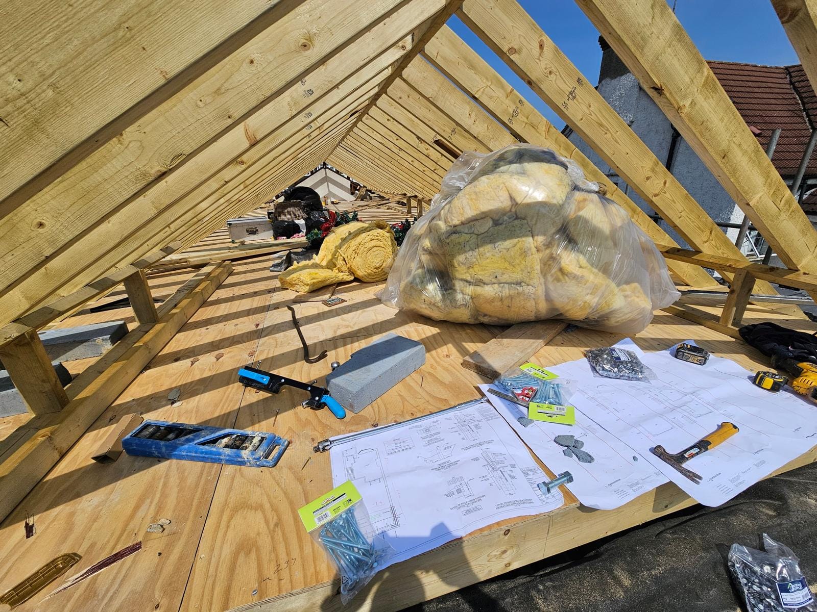 Roof structure drawings, tools and fixings laid on the new plywood deck beneath the rafters, with insulation bagged up.