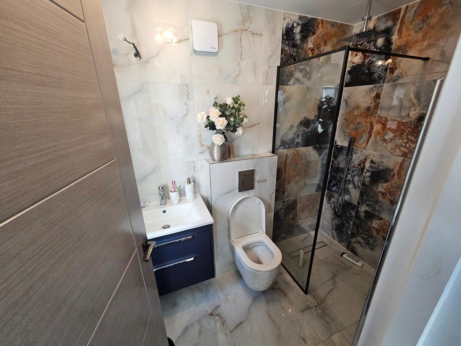 Shower room with a navy wall-hung vanity, wall-hung WC and a walk-in shower lined in onyx-effect tiles.