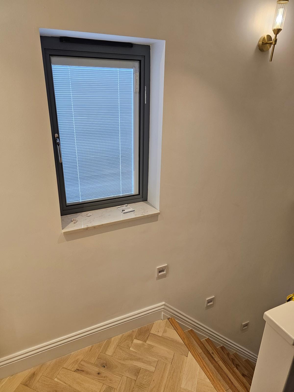 Stairwell with a grey aluminium window with integral blinds, a marble-effect sill and a brass wall light.