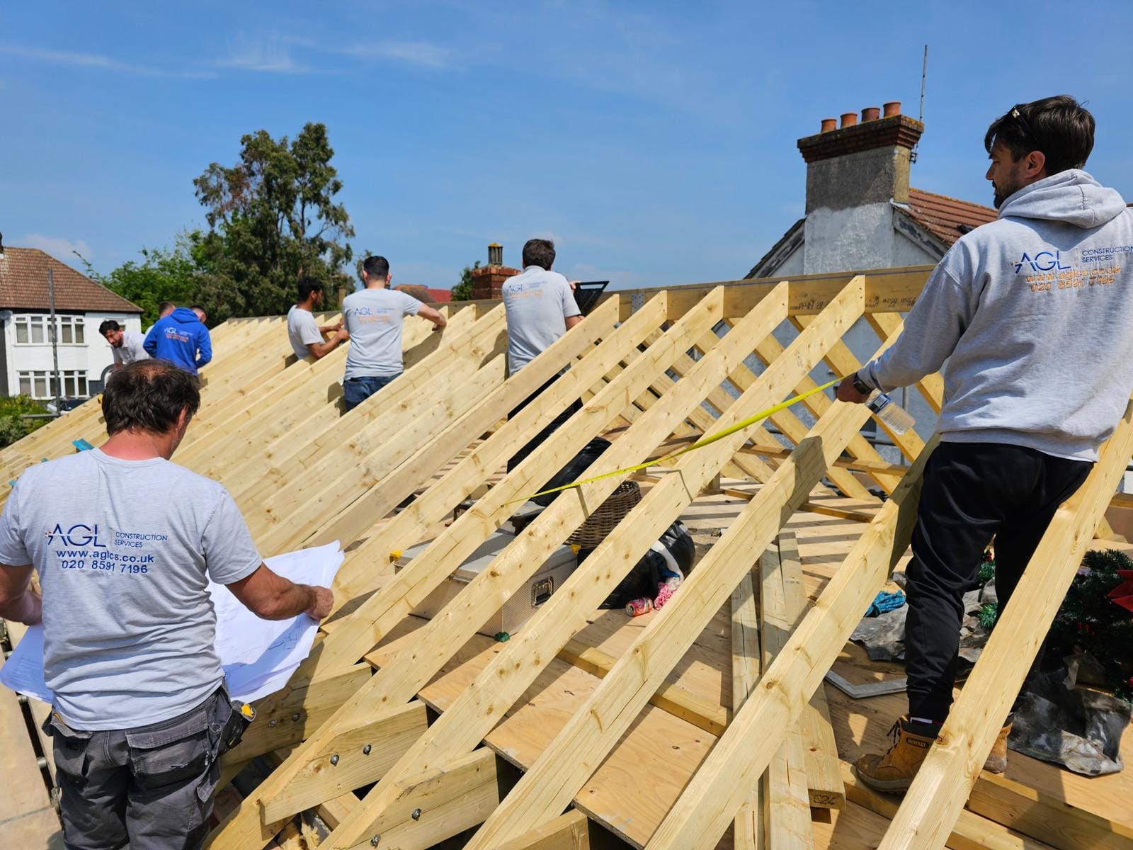 AGL team measuring and setting out the new rafters, one holding drawings, with a tape stretched across the timbers.