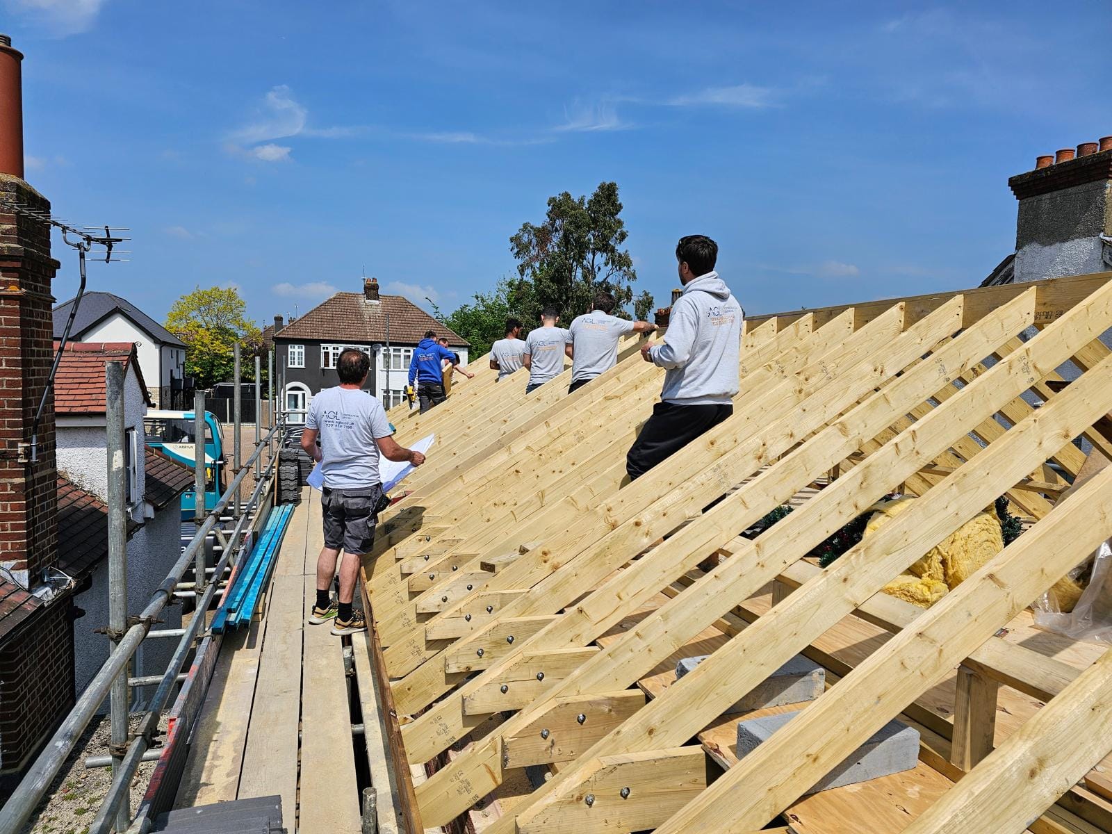 AGL team walking along the new timber rafters between two chimney stacks, with suburban rooftops behind.
