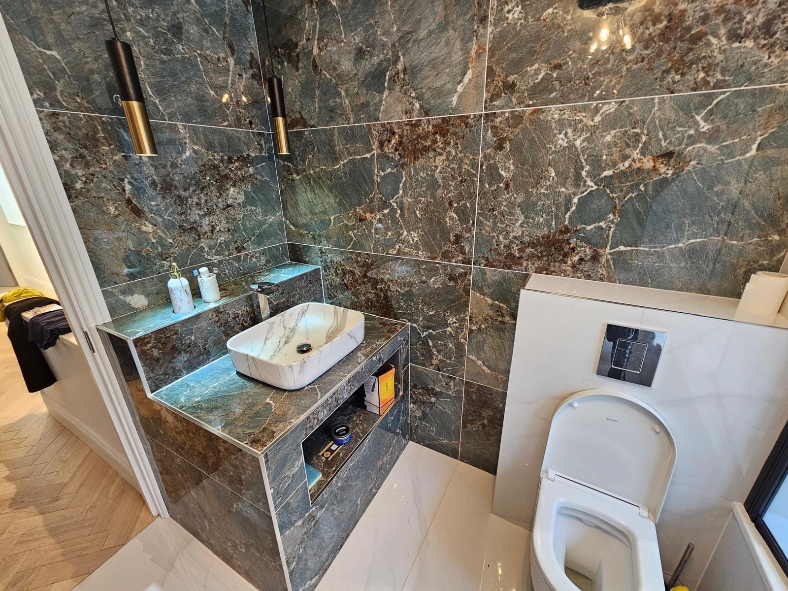 Vessel basin on a dark-green marble-effect plinth with gold pendant lights, beside a wall-hung WC with concealed cistern.