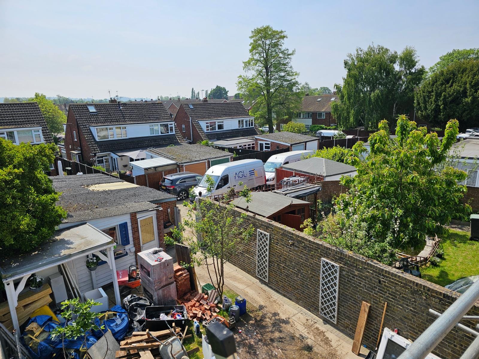 View from the scaffold over back gardens and a side garden stacked with materials, with AGL vans beyond.