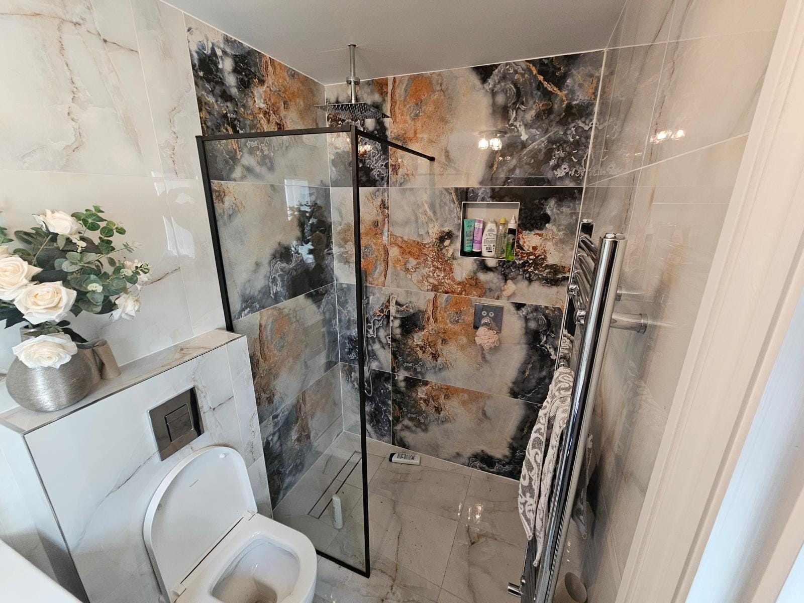Walk-in shower with a black-framed glass screen, rain shower head and onyx-effect wall tiles beside a wall-hung WC.
